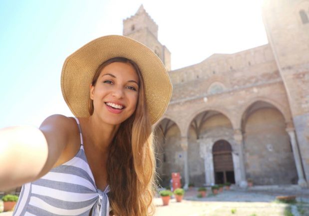 Smiling woman take selfie with Cefalu Cathedral in Sicily, Italy